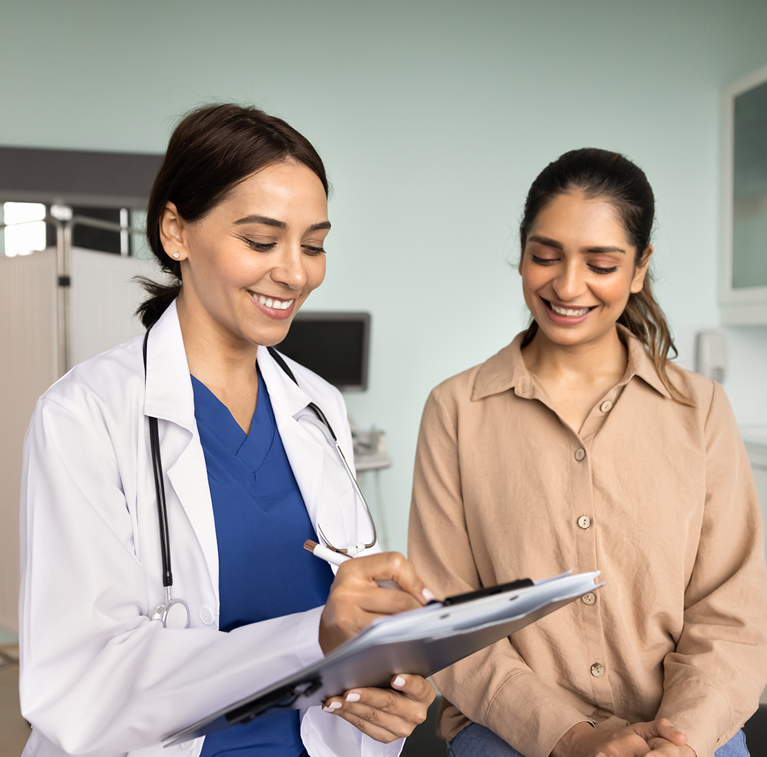 female doctor in labcoat and blue undershirt holding a clipboard and speaking to patient