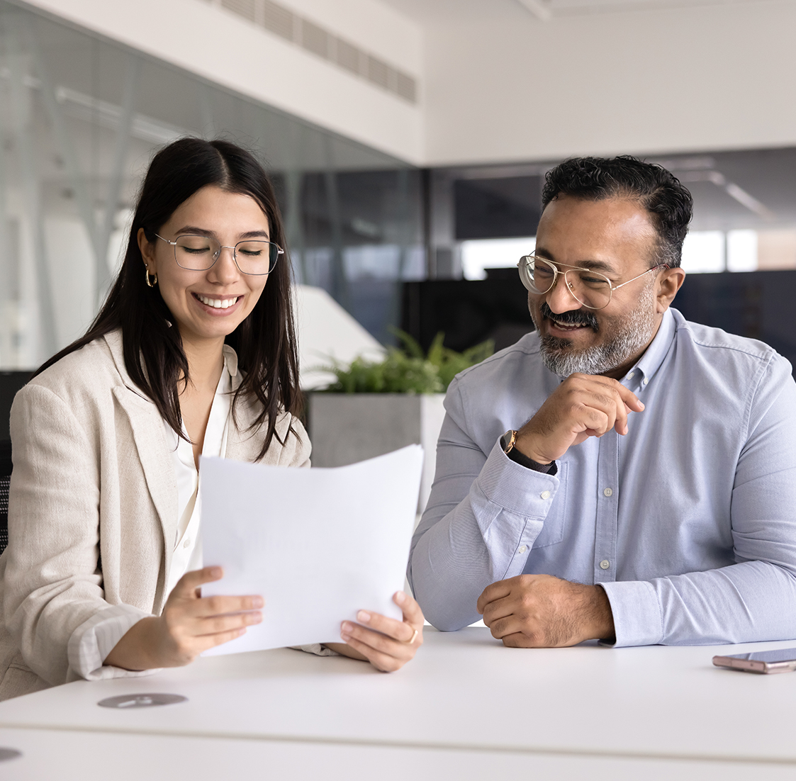 smiling woman holding paper while male at table next to her looks on